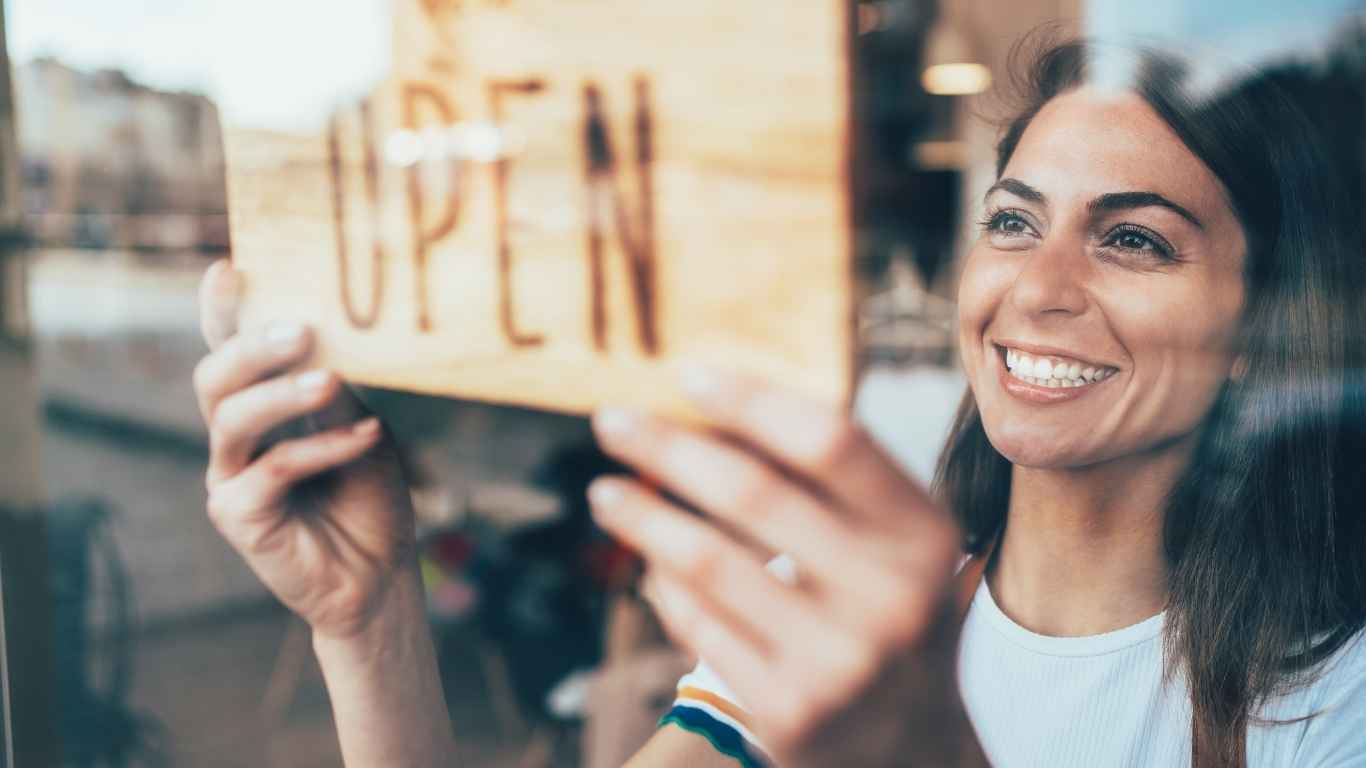 brunette woman holding up an open sign.